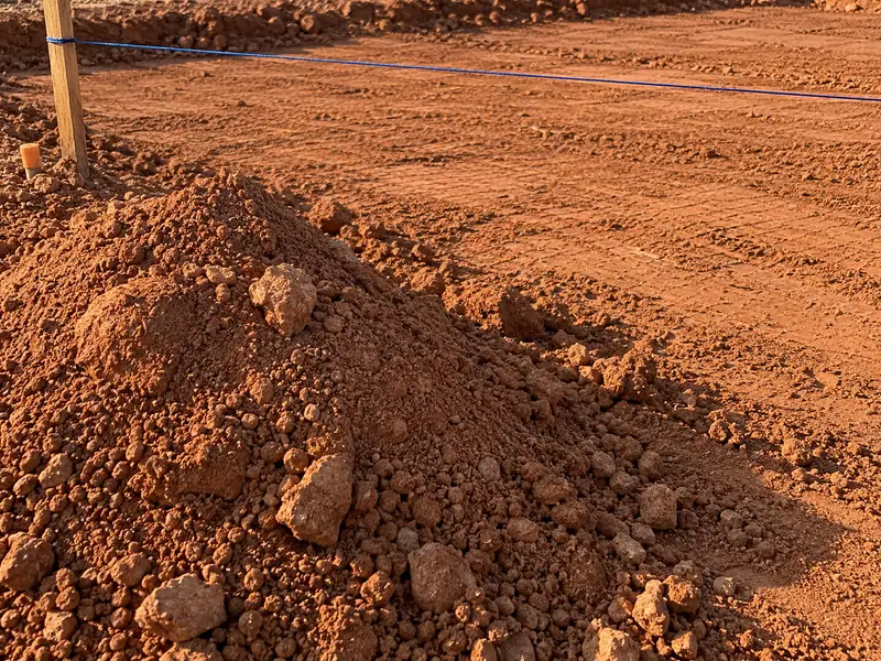 Monte de solo mineral solto junto a uma camada de aterro espalhada e linha de referência no terreno